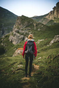 Rear view of woman with umbrella walking on mountain against sky