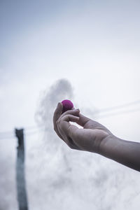 Close-up of hand holding purple firework against sky