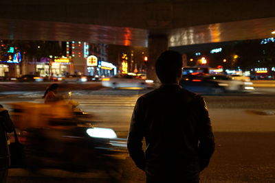 Rear view of man standing on road at night