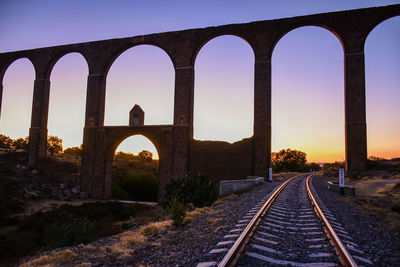 Arch bridge over railroad tracks against clear sky