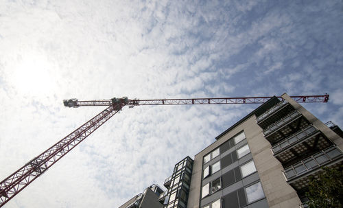 Low angle view of crane by building against sky