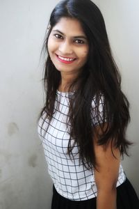 Portrait of smiling young woman standing against wall