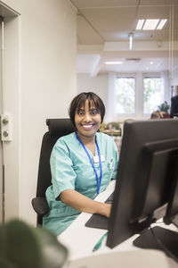 Portrait of smiling female doctor with bangs working on computer while sitting in clinic