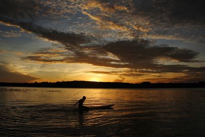 Silhouette person on sea against sky during sunset