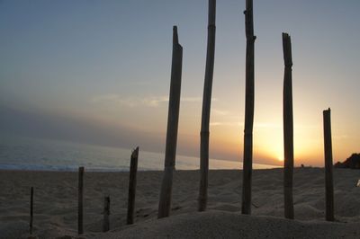 Wooden posts on beach against sky during sunset