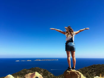 Man standing on rock by sea against clear blue sky