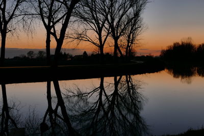 Silhouette bare trees by lake against sky during sunset