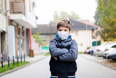 Kid with arms crossed standing on the street and wearing kn95 face mask due to covid-19 pandemic.