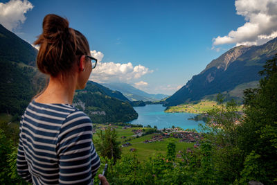 Woman looking at lake and mountains against blue sky