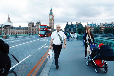 People walking on westminster bridge by big ben against cloudy sky