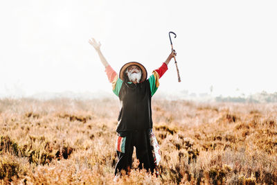 Cheerful old ethnic rastafari with dreadlocks looking up celebrating victory while standing in a dry meadow in the nature