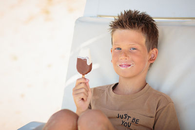 Handsome boy sitting on the beach and eating ice cream