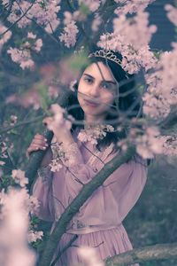 Portrait of young woman wearing crown standing by pink flowering tree