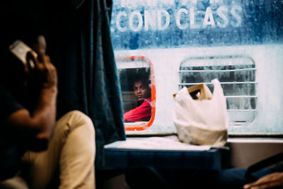 Reflection of man using mobile phone while sitting in bus