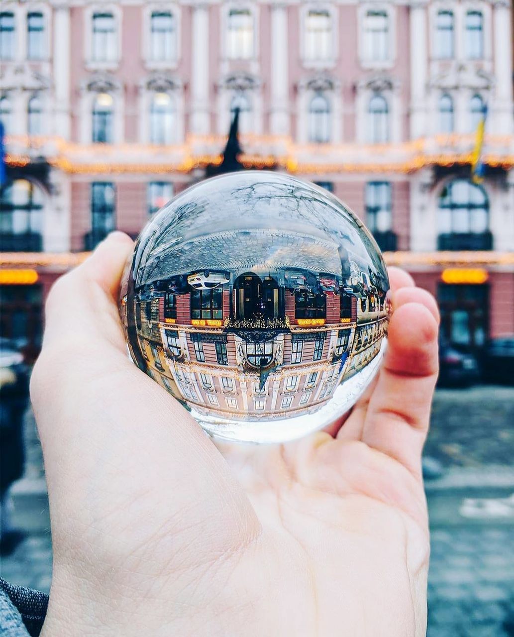 architecture, holding, hand, city, building exterior, one person, built structure, sphere, focus on foreground, blue, day, outdoors, close-up, adult, city life, nature, reflection, world, travel destinations, water, art, crystal ball, travel, ball