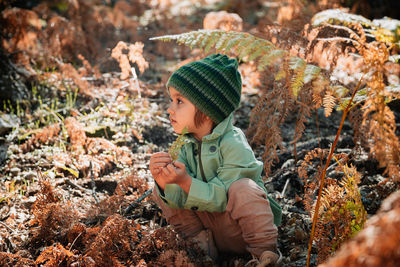 Girl looking away while crouching on leaves in forest