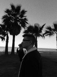 Portrait of young man standing by palm trees on beach