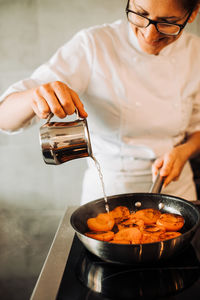 Female chef is adding water to cooking apricots