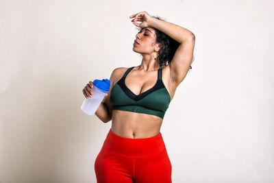 Young woman holding water bottle standing against white background