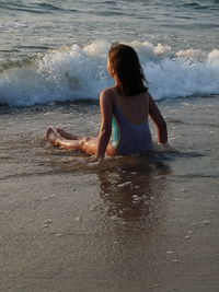 Rear view of girl sitting on shore at beach