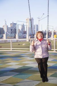 Full length of smiling woman swinging in city