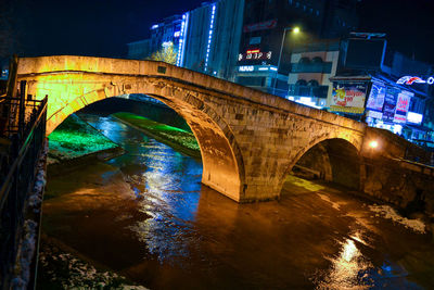 Arch bridge over river in city at night