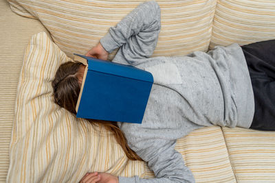 High angle view of woman with book on face lying on sofa at home