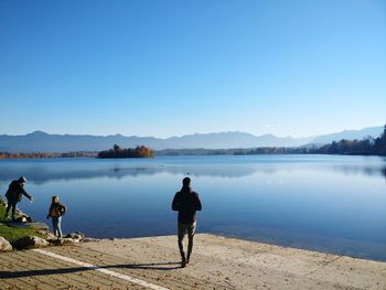 Rear view of man looking at lake against clear blue sky