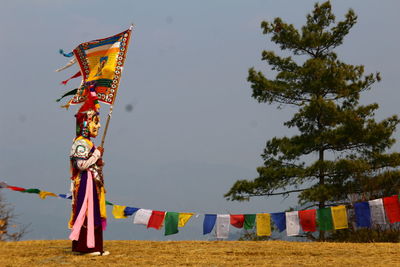 Side view of person wearing costume while standing by colorful prayer flags on land