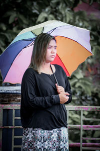 Portrait of young woman with umbrella standing in city