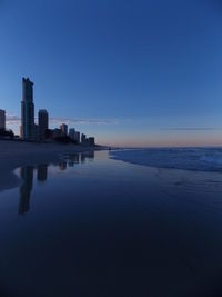 Buildings reflection on wet shore at surfers paradise against sky