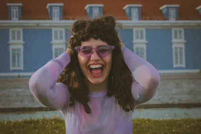 Woman with hand in hair shouting while standing against building