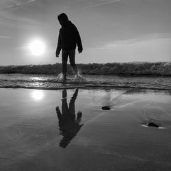 Rear view of man standing at beach against sky