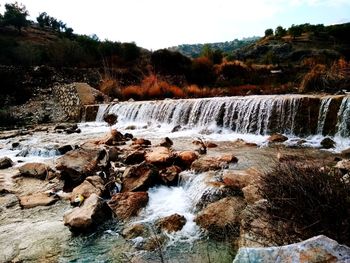 Scenic view of waterfall in forest against sky