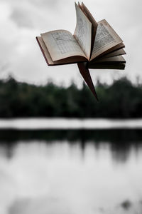Close-up of open book by lake against sky