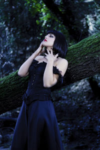 Young woman standing by tree trunk in forest