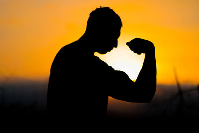 Silhouette woman standing against orange sky during sunset