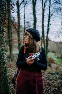 Young woman holding camera while standing in forest
