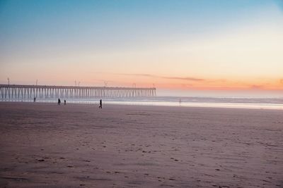 Pier on beach against sky during sunset