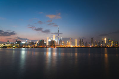 Illuminated buildings by river against sky at night