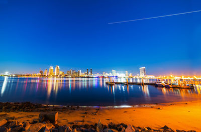 Illuminated city by sea against clear sky at dusk