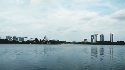 View of buildings by river against cloudy sky