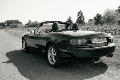 Vintage car on field by road against clear sky