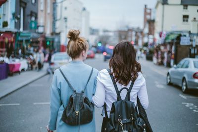 Rear view of female friends walking on road in city