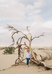 Woman sitting on dead tree against sky