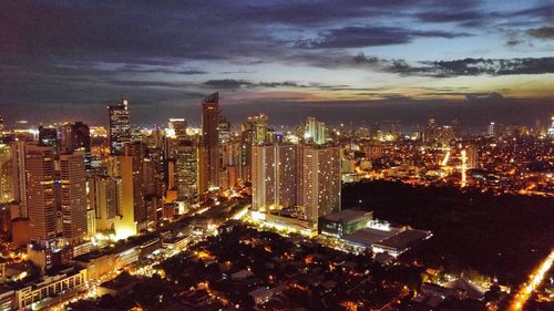 Illuminated buildings in city against cloudy sky