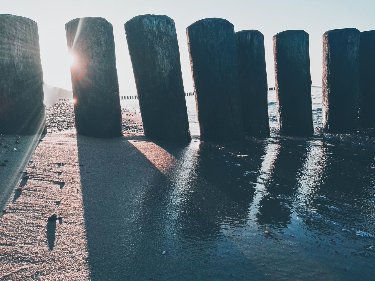 water, sunlight, nature, no people, sky, shadow, sea, day, side by side, in a row, tranquility, outdoors, beach, post, land, tranquil scene, scenics - nature, beauty in nature, architecture, wooden post