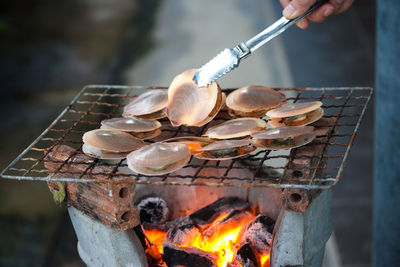 Cropped hand with mussels on barbecue grill