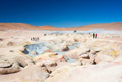 People by mud pots on landscape against clear sky