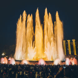 Crowd watching huge fountain against sky at night